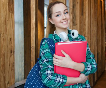 Smiling student holding book and wearing headphones, ready for study.