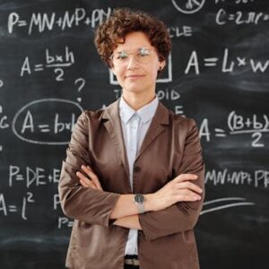 Confident female teacher standing with arms crossed in front of a detailed mathematical blackboard.