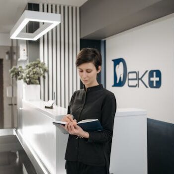 Female receptionist writing notes at dental office reception. Professional healthcare setting.