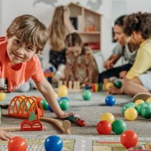 Happy children and a caregiver playing with colorful toys in a lively indoor playroom setting.