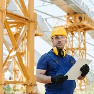 Worker in safety gear inspecting construction site with clipboard.