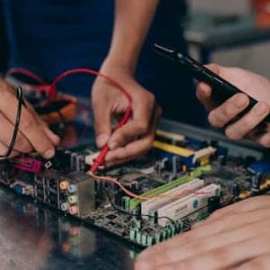 Close-up of hands working on a motherboard using electrical tools and tester.